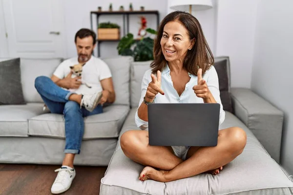Hispanic Middle Age Couple Home Woman Using Laptop Pointing Fingers — Stok Foto