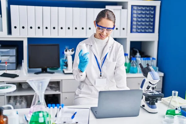 Young woman scientist smiling confident holding pills at laboratory