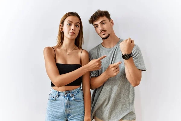 Young Beautiful Couple Standing Together Isolated Background Hurry Pointing Watch — Zdjęcie stockowe