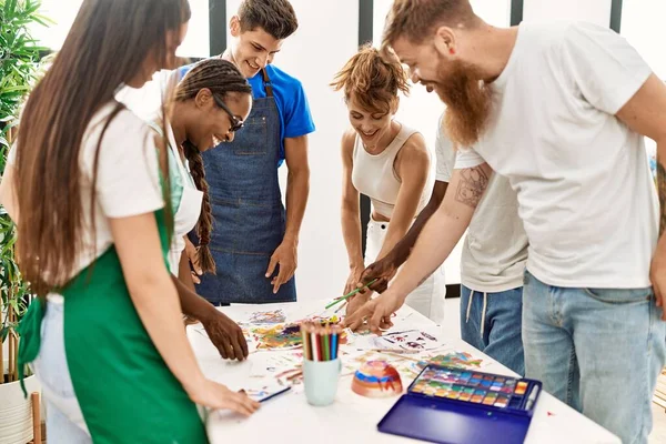 Group of people smiling happy drawing standing around the table at art studio.