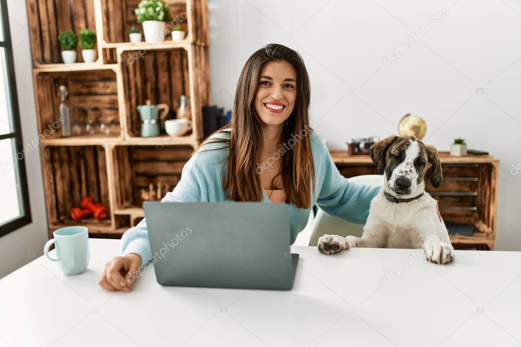 Young woman using laptop sitting on table with dog at home