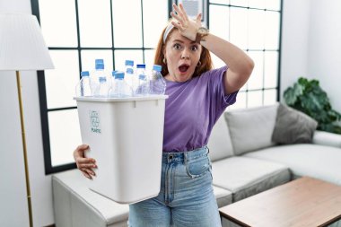 Geri dönüşüm sepetini elinde tutan kızıl saçlı genç bir kadın. Elinde plastik şişeler var. Yanlışlıkla el üstünde şaşırmış. Hatayı hatırla. Unuttum, kötü hafıza kavramı. 