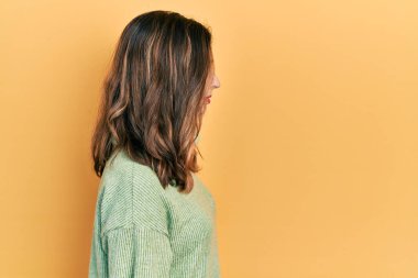 Latin kökenli genç bir kız günlük giysiler giyiyor. Yan tarafa bakıyor, rahat poz veriyor, kendine güvenen bir gülümsemeyle doğal bir yüz ifadesi sergiliyor.. 