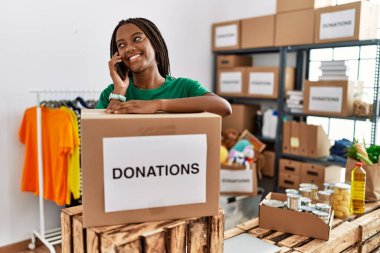 Gönüllü üniforma giyen genç Afro-Amerikan kadın yardım merkezindeki akıllı telefondan konuşuyor.