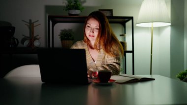Young redhead woman using laptop studying at home