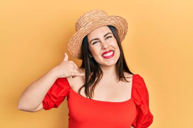 Yaz şapkası takan, gülümseyen, el ve parmaklarıyla telefonla konuşan İspanyol bir kadın. iletişim kavramları. 