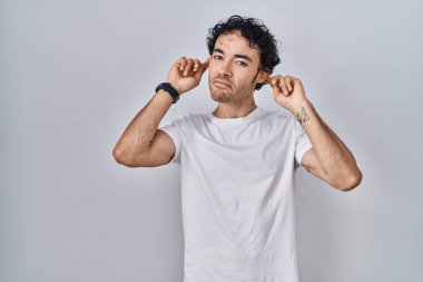 Hispanic man standing over isolated background smiling pulling ears with fingers, funny gesture. audition problem 