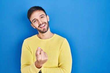 Mavi arka planda dikilen İspanyol adam seni buraya çağırıyor. El kol hareketi yap. Mutlu ve gülümseyen bir şekilde karşıla. 