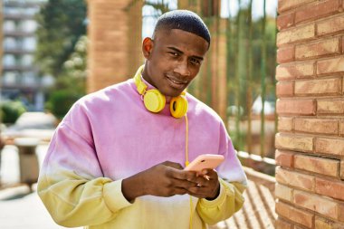 Genç Afrikalı Amerikalı adam şehirde akıllı telefon kullanarak mutlu bir şekilde gülümsüyor..