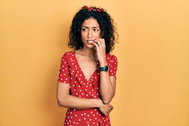 Yazlık elbise giyen genç Latin kız gergin ve gergin görünüyor. Ağzı tırnak yiyen ellerle. anksiyete. 