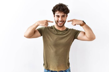 Hispanic man standing over isolated white background smiling cheerful showing and pointing with fingers teeth and mouth. dental health concept. 