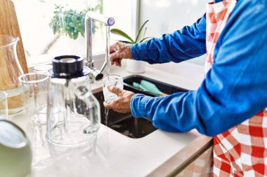 Kıdemli adam mutfakta cam yıkıyor.