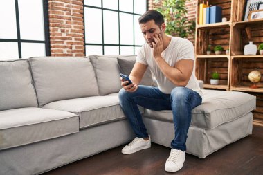 Evdeki kanepede oturan, akıllı telefon kullanan genç bir İspanyol.