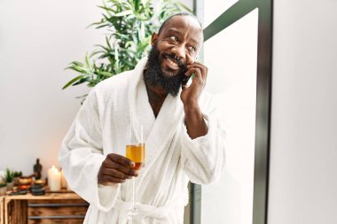 Genç Afro-Amerikalı adam akıllı telefondan konuşuyor güzellik merkezinde şampanya içiyor.