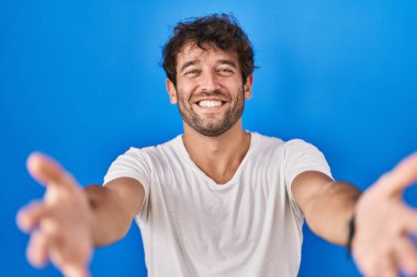 Mavi arka planda duran Latin asıllı genç adam gülümseyerek yardım ve kabullenme eli uzatıyor.. 