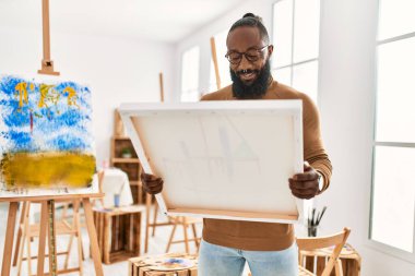 Genç Afrikalı Amerikalı ressam resim stüdyosunda tuval tutarken mutlu gülümsüyor..
