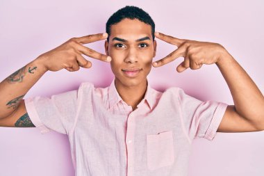 Genç Afrikalı Amerikalı adam zafer işareti yapıyor ve barış jesti yüzünde ciddi bir ifadeyle rahatladı. Basit ve doğal bir şekilde kameraya bakıyorsun.. 