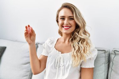 Adet bardağı tutan genç bir kadın evdeki kanepede oturuyor.