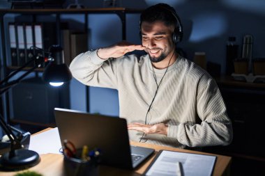 Genç yakışıklı adam geceleri bilgisayar bilgisayarı kullanarak çalışıyor. Elleri büyük ve büyük boy işareti, ölçü sembolü gösteriyor. Kameraya bakıp gülümsüyor. ölçüm kavramı. 