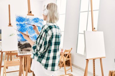 Young artist student girl on back view painting and listening music at art studio.
