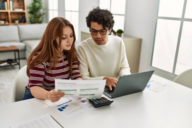 Ciddi ifadeleri olan genç bir çift evde masada dizüstü bilgisayar kullanıyor..