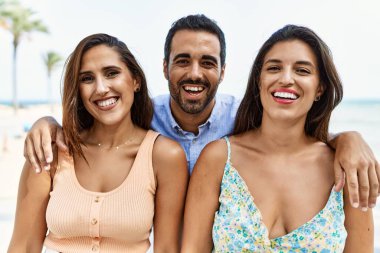 Mutlu gülümseyen ve kumsalda sarılan üç İspanyol genç arkadaş..