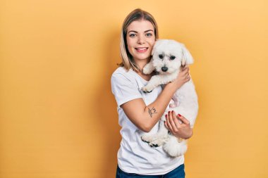 Güzel beyaz kadın sevimli köpeğe sarılıyor pozitif ve mutlu görünüyor ve gülümsüyor kendine güvenen bir gülümsemeyle dişlerini gösteriyor. 