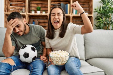 Genç latin çift evde futbol maçı izleyip porpcorn yiyorlar..