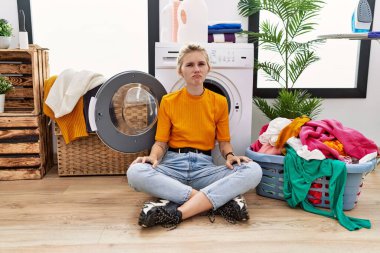 Young blonde woman doing laundry sitting by washing machine depressed and worry for distress, crying angry and afraid. sad expression. 