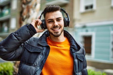 Sakallı yakışıklı, neşeli ve kendine güvenen, kışlık palto ve kulaklık takan bir İspanyol.