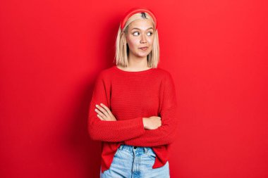 Beautiful blonde woman wearing casual red sweater smiling looking to the side and staring away thinking. 