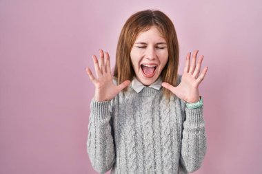 Beautiful woman standing over pink background celebrating mad and crazy for success with arms raised and closed eyes screaming excited. winner concept 