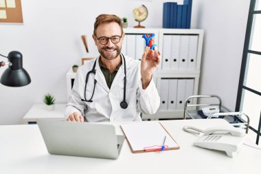 Klinikte kalbi tutan, doktor üniforması giyen orta yaşlı İspanyol bir adam.