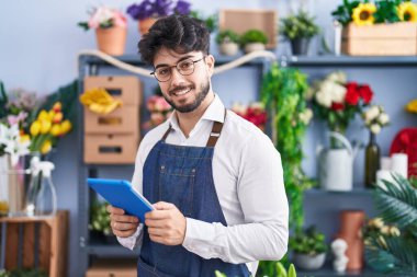 Young hispanic man florist smiling confident using touchpad at florist shop