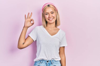 Beautiful blonde woman wearing casual white t shirt smiling positive doing ok sign with hand and fingers. successful expression. 
