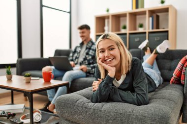 Evdeki kanepede oturup dizüstü bilgisayar kullanarak gülümseyen beyaz bir çift..