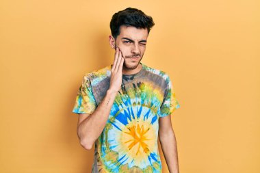 Günlük kıyafetler giyen genç İspanyol adam diş ağrısı ya da diş hastalığından dolayı acı dolu bir ifadeyle ağıza dokunuyor. dişçi 