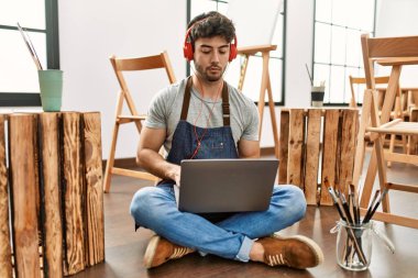 Sanat stüdyosunda kulaklık ve dizüstü bilgisayar kullanan İspanyol genç bir sanatçı..