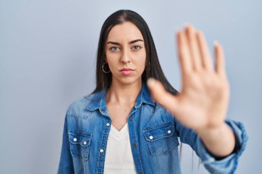 Hispanic woman standing over blue background doing stop sing with palm of the hand. warning expression with negative and serious gesture on the face. 