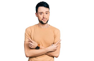 Her iki tarafı parmaklarıyla gösteren günlük tişörtlü, sakallı İspanyol adam farklı yönlere bakıyor. 