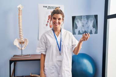 Young woman holding pelvis radiography looking positive and happy standing and smiling with a confident smile showing teeth 