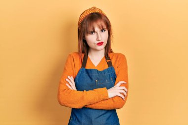 Önlük giymiş, kuşkucu ve gergin genç bir kadın. Yüzünde çapraz kollu tasvip etmeyen bir ifade. negatif kişi. 
