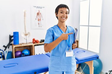 Kısa saçlı, İspanyol bir kadın ağrı kesici kliniğinde çalışıyor. Arka tarafı işaret ediyor. El ve baş parmakları havada, kendine güvenen. 