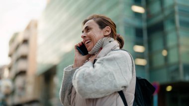 Orta yaşlı İspanyol kadın gülümsüyor. Akıllı telefondan konuşuyor.