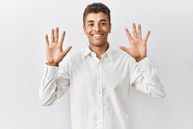 Soyutlanmış arka planda duran yakışıklı İspanyol adam on numarayı gösterip işaret ederken kendinden emin ve mutlu bir şekilde gülümsüyor.. 