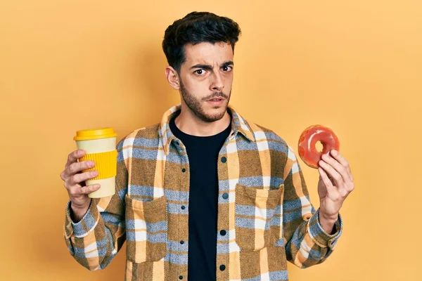 Joven Hispano Comiendo Donuts Bebiendo Café Expresión Despistada Confusa Concepto —  Fotos de Stock