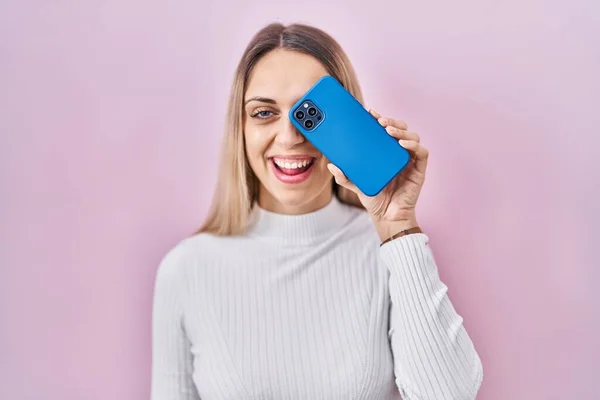 Young Blonde Woman Holding Smartphone Covering Eye Looking Positive Happy — Stock Photo, Image