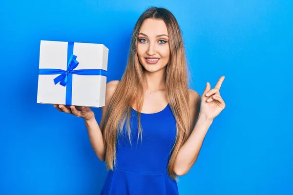 Joven Chica Rubia Sosteniendo Regalo Sonriendo Feliz Señalando Con Mano — Foto de Stock