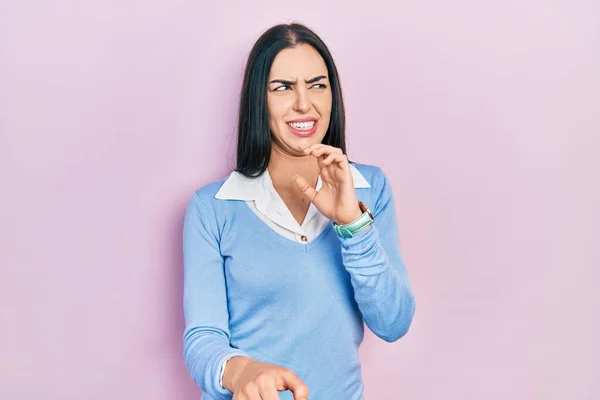 Beautiful woman with blue eyes standing over pink background disgusted expression, displeased and fearful doing disgust face because aversion reaction. with hands raised
