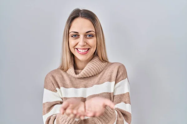 Young blonde woman wearing turtleneck sweater over isolated background smiling with hands palms together receiving or giving gesture. hold and protection